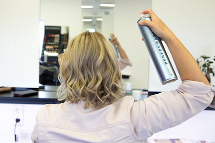 Frau fixiert Beach Waves mit Haarsprray